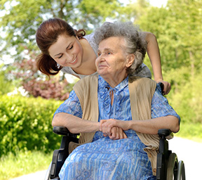 Pflegekraft schiebt demenzkranke ältere Dame im Rollstuhl
